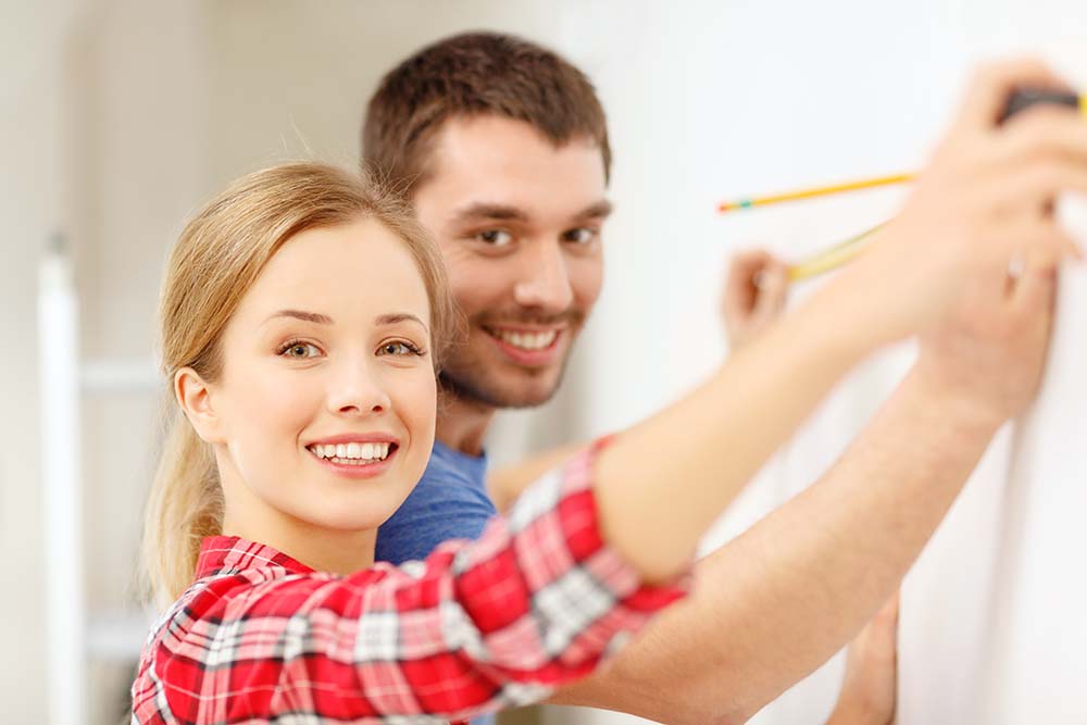 repair, building and home concept - smiling couple measuring wall